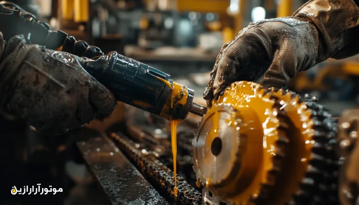 روغنکاری زنجیر و چرخدنده صنعتی با استفاده از گریس غلیظ؛ تکنسینی با دستکش ایمنی در حال اجرای فرآیند روانکاری در محیط کارخانه