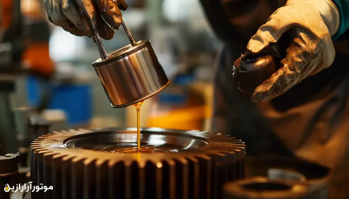 نمای نزدیک از دستکش‌های صنعتی در حال اعمال روغن روانکار بر سطح چرخ‌دنده بزرگ با استفاده از ظرف فلزی، در فضای کارگاه تخصصی.